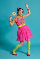 Lovely girl with a multi-colored braids hairstyle and bright make-up, posing in studio against a blue background, holding a lollipop in her hand. photo