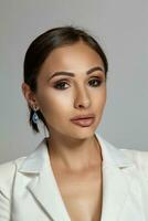 Close up portrait of a brunette model girl with professional evening make-up, wearing a white jacket with black bra, posing on gray background. photo