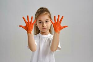 pequeño niña en blanco camiseta es posando en pie aislado en blanco y gesticulando con su pintado en diferente colores palmas Arte estudio. de cerca. foto