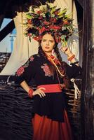 Brunette girl in a white ukrainian authentic national costume and a wreath of flowers is posing against a terrace. Close-up. photo