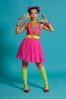 Lovely girl with a multi-colored braids hairstyle and bright make-up, posing in studio against a blue background, holding a lollipop in her hand. photo