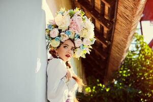 Brunette girl in a white ukrainian authentic national costume and a wreath of flowers is posing against a white hut. photo