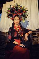 Brunette girl in a black and red embroidered ukrainian authentic national costume and a wreath of flowers is posing against a terrace. Close-up. photo