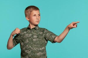 Close-up portrait of a blonde teenage boy in a green shirt with palm print posing against a blue studio background. Concept of sincere emotions. photo