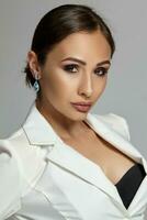 Close up portrait of a brunette model girl with professional evening make-up, wearing a white jacket with black bra, posing on gray background. photo