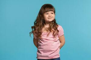 hermosa pequeño niña vistiendo en un rosado camiseta es posando en contra un azul estudio antecedentes. foto