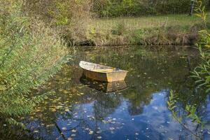 esta fotos muestra un barco en un pequeño estanque con reflexiones en un agricultores pueblo en Alemania