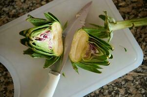 Two halves of fresh ripe organic artichoke and a kitchen knife on cutting board, on marble stone kitchen counter photo