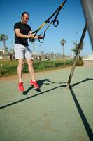 Athletic man working out with suspension straps, doing jumping exercises in the urban sports ground photo