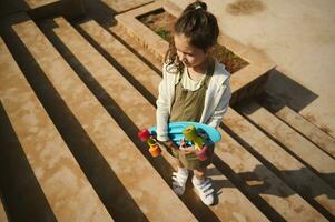 Overhead view of a cute little child girl standing on steps with a skateboard in her hands. Childhood, Leisure activity photo