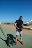 lleno longitud retrato de un masculino atleta Listo para un peso corporal formación al aire libre, en urbano Deportes suelo en soleado día foto