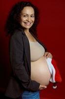 Charming pregnant pretty woman holding Santa hat over her naked big belly, expressing positive emotions at camera photo