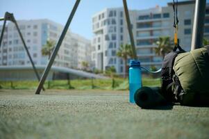 Sports tools on the sports ground. A backpack, bottle of water and rolled fitness mat. Sport. Fitness. Copy ad space photo