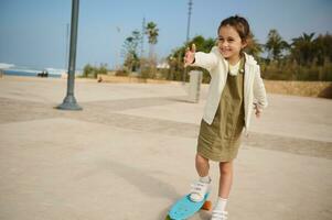 Happy elementary age child girl smiling cutely, enjoying skateboarding on a skatepark on beautiful sunny day. photo