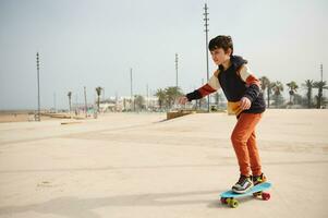 Happy active teenage boy riding on skateboard on an urban skatepark playground, dressed in stylish sportswear. photo