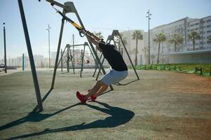 Handsome determined athletic man exercising outdoors with suspension fitness straps. People and sport concept photo