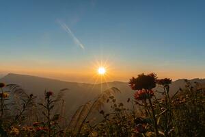 Sunset above horizon line with sun setting down behind mountains. photo