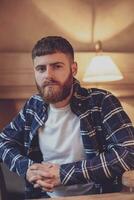 Portrait handsome bearded man wearing plaid shirt at modern cafe photo