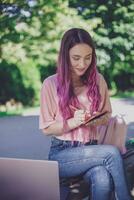 mujer escritura en un cuaderno sentado en un de madera banco en el par foto