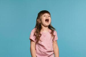 Beautiful little girl wearing in a pink t-shirt is posing against a blue studio background. photo