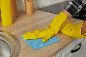 Hands in gloves with green rag is cleaning kitchen cabinets - housework and housekeeping concept photo