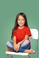 pequeño niña vistiendo rojo t-corto y posando en silla foto