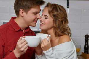 Happy young lovely couple on kitchen hugging each other. They enjoy drinking coffee photo