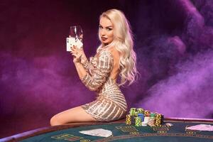 Blonde woman with a perfect hairstyle and bright make-up is posing with playing cards in her hands. Casino, poker. photo