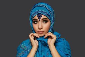 Studio shot of a young beautiful woman wearing the blue hijab decorated with sequins and jewelry. Arabic style. photo