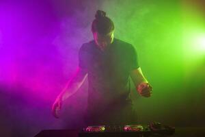 DJ at work mixing sound on her decks at a party or night club with colourful smoke light background photo