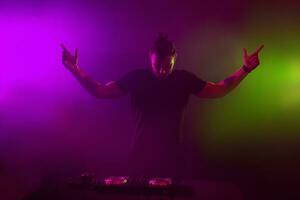 DJ at work mixing sound on her decks at a party or night club with colourful smoke light background photo