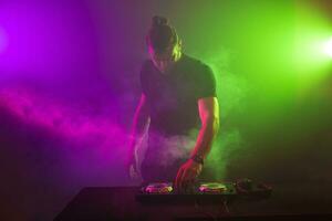 DJ at work mixing sound on her decks at a party or night club with colourful smoke light background photo