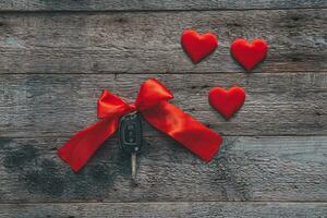 Car keys with red ribbon and heart on wooden background. The concept of a car gift for the holiday of February 14th. Valentine's Day. photo