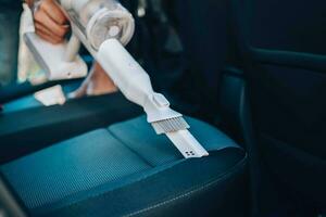 Close-up of a man vacuuming a car seat. The hand holds a cordless vacuum cleaner and cleans the interior of the car. photo