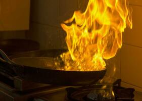 Chef cooking and doing flambe on food in a restaurant kitchen. Close up photo