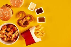 Fast food dish top view. French fries, hamburger, mayonnaise and ketchup sauces on yellow background. photo