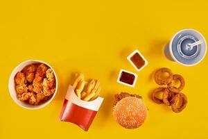 Fast food dish top view. French fries, hamburger, mayonnaise and ketchup sauces on yellow background. photo