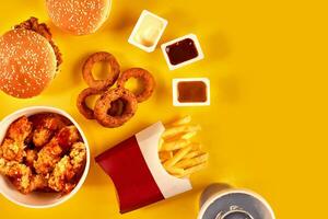 rápido comida plato parte superior vista. francés papas fritas, hamburguesa, mayonesa y salsa de tomate salsas en amarillo antecedentes. foto