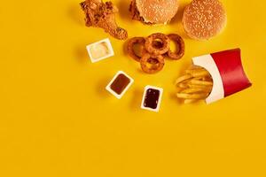 rápido comida plato parte superior vista. francés papas fritas, hamburguesa, mayonesa y salsa de tomate salsas en amarillo antecedentes. foto