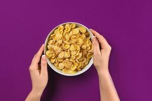 Female hands holding bowl with healthy breakfast, closeup. Bowl with cornflakes on the colorful background photo