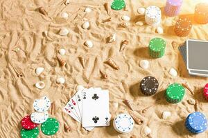 Gambling on vacation concept - white sand with seashells , colored poker chips and cards. Top view photo