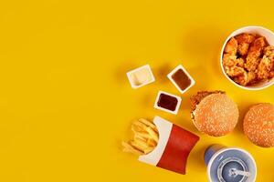 Fast food dish top view. French fries, hamburger, mayonnaise and ketchup sauces on yellow background. photo