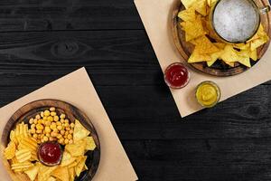Lager beer and snacks on black wooden table. Nuts, chips. Top view with copyspace photo