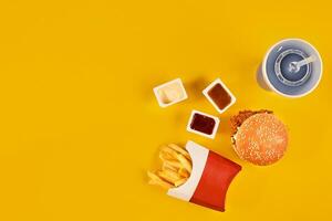 Fast food dish top view. Meat burger, potato chips and wedges. Take away composition. French fries, hamburger, mayonnaise and ketchup sauces on yellow background. photo