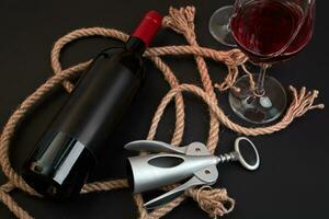 Red wine bottle, two glasses and corkscrew on black background. Top view photo