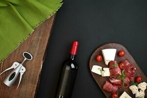 Wine bottle with cheese and traditional sausages on wooden board on black background with copy space photo