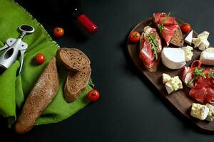 Wine bottle with cheese and traditional sausages on wooden board on black background with copy space photo