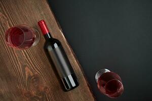 Bottle of wine and two glasses on the wooden board on black background. Top view with copy space photo