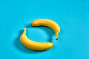 Two yellow ripe bananas on blue background with space for text or design. Top view photo