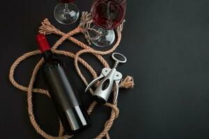Red wine bottle, two glasses and corkscrew on black background. Top view with copy space photo